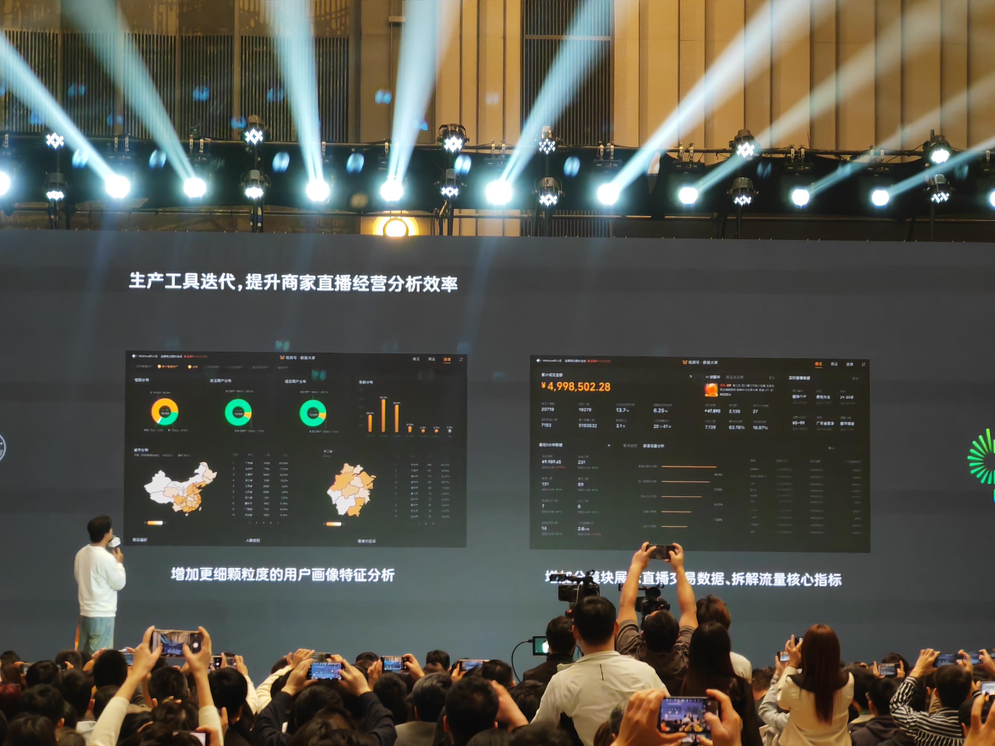 图片展示的是2024「微信公开课」现场，台上演讲者身后的屏幕显示“生产工具迭代，提升商家直播经营分析效率”。屏幕左侧呈现增加更细颗粒度的用户画像特征分析图表，包括环形图和地图等；右侧展示直播交易数据、拆解流量核心指标等内容，屏幕上还显示了金额“¥4,998,502.28”。台下众多观众正举起手机拍摄。此图与上文视频号直播带货分享会中提到的完善后台数据等内容相关。
