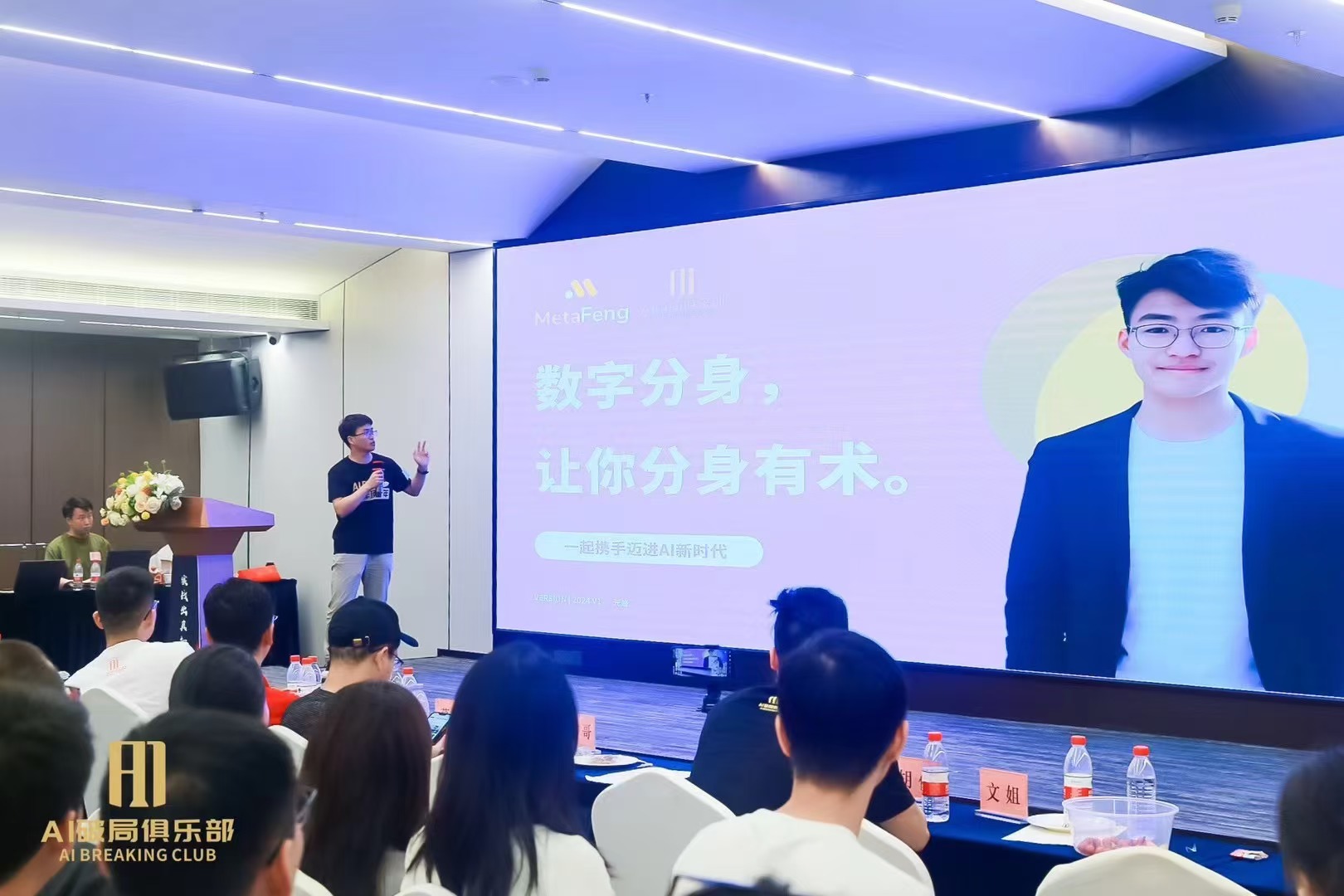 图片展示的是2024年9月破局行动家大会现场。画面中，一位男士在台上演讲，身后大屏幕上显示“数字分身，让你分身有术”及一张男子照片。台下观众席坐满了人，部分观众戴着眼镜，有的低头看手机。台前有摆放水瓶的桌子，桌上还放着“AI破局俱乐部”的标识。此图与上文提到的作者在大会上分享《AI数字人，AIP路上的加速器》内容相契合，直观呈现了演讲场景。