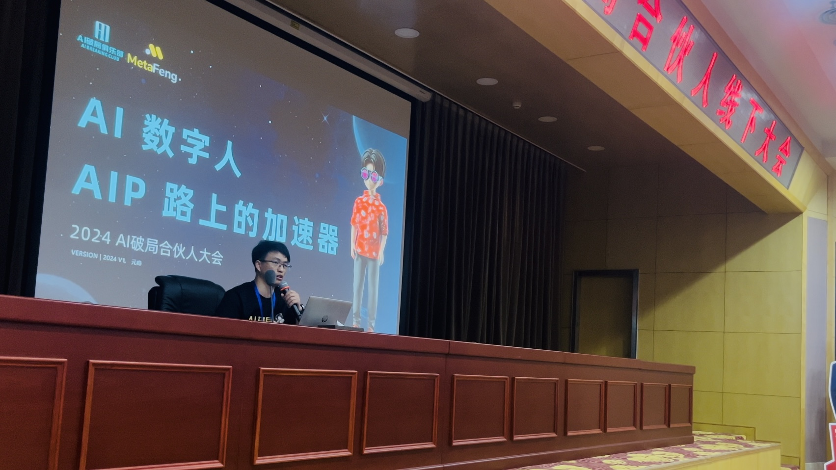 图片展示的是2024 AI破局合伙人大会现场，一位男士在台上演讲。背景大屏幕上显示“AI数字人 AIP路上的加速器”及“2024 AI破局合伙人大会”字样，旁边有一个穿着红白格子衬衫的卡通人物形象。男士戴眼镜，手持麦克风，专注地对着屏幕讲话。画面右侧有“合伙人线下大会”的红色标识。此图与文档中作者分享在该大会上演讲《AI数字人，AIP路上的加速器》的内容相契合，呈现了演讲现场情况。