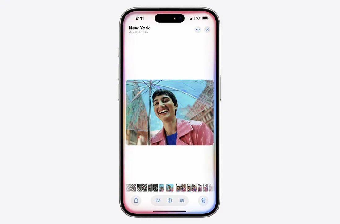 图片展示了一部iPhone屏幕，显示时间为9:41，地点为New York。屏幕上有一张照片，照片中一位穿着粉色外套、蓝色内搭的人在雨中笑得很开心，背景是城市街景。屏幕下方有多个小图标，包括相机、表情符号、画笔等。该图片与上下文紧密相关，直观呈现了新的Siri能够自己操作，通过Ferret-UI视觉语言模型看懂iOS屏幕上的图标、小部件和文字，还能搞明白它们之间的关系和作用这一功能。