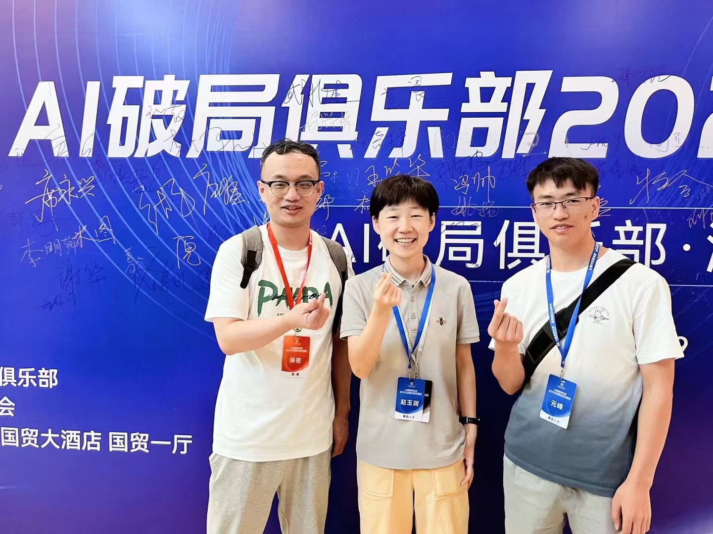 图片展示了北京线下大会的场景，三位参与者站在“AI破局俱乐部2023”背景前合影。中间的女性穿着灰色T恤和浅色裤子，面带微笑，比出“V”字手势；两侧的男性分别穿着白色和灰色T恤，均佩戴证件。背景板上有“AI破局俱乐部”字样及“国贸大酒店 国贸一厅”等信息，还写有“精华文章（7颗）”等字样。此图与文档中北京线下大会和潘神、玉润等伙伴面基的内容相呼应，体现了线下交流的氛围。