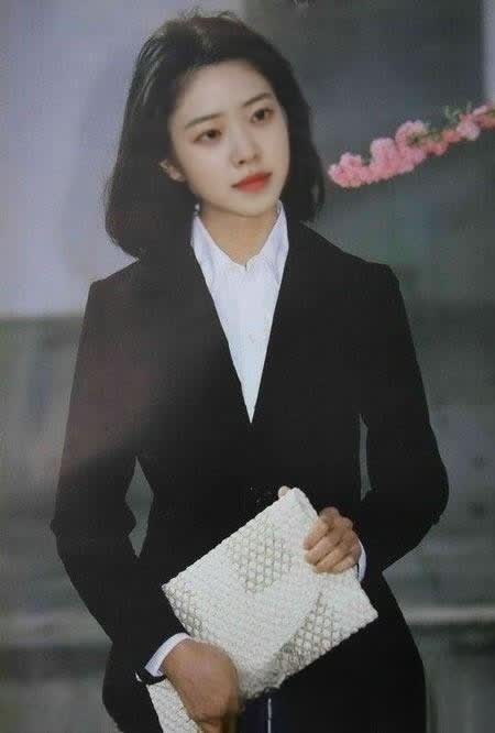 图片展示了一位穿着黑色西装、白色衬衫的女性，她手持白色手包，背景模糊，有粉色花朵装饰。该图片位于介绍“图片高清化”步骤的上下文中，用于说明旧的老照片（左图）在高清放大处理后（右图）的效果对比，直观呈现了高清化处理前后的视觉差异，帮助理解高清化技术在修复老照片方面的应用。
