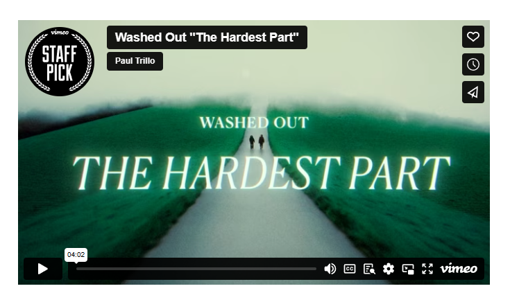 图片展示的是音乐视频《The Hardest Part》的封面，由Washed Out乐队制作。画面中，一条蜿蜒的白色小路延伸至远方，两侧是绿色的草地，路中央有两个人影。画面顶部有“Washed Out 'The Hardest Part'”及“Paul Trillo”字样，左上角有“STAFF PICK”标识。右上角有心形、钟表、喇叭图标。底部有播放按钮、时间显示“04:02”及Vimeo标志。该图片与上下文介绍的视频内容相契合，直观呈现了视频主题及风格。